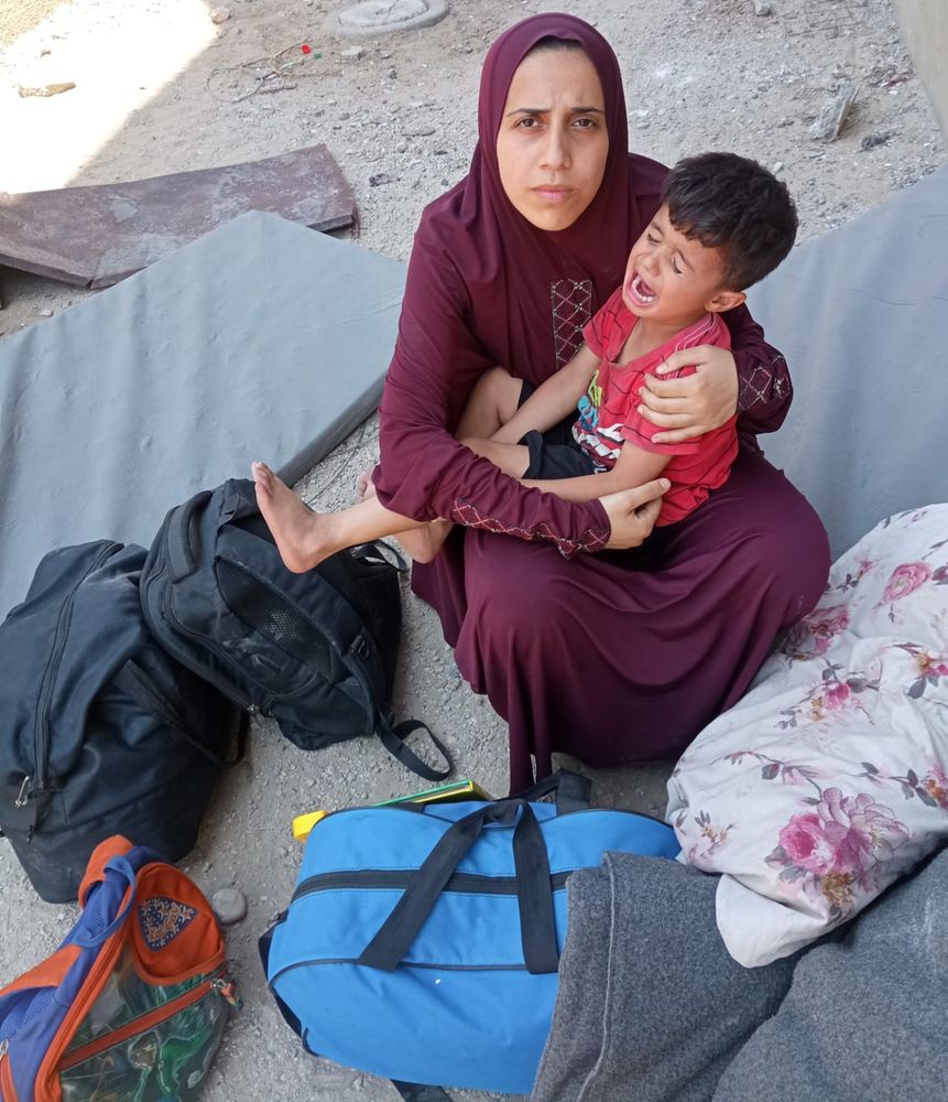 A Palestinian mother cradles her crying son as she sits on the bare ground surrounded by the bags that contain their few remaining possessions.