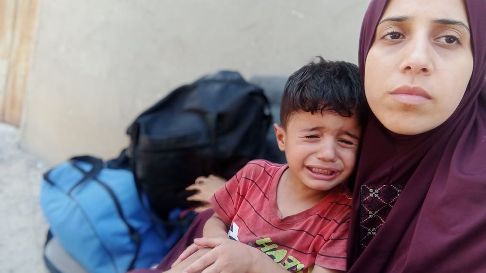 A Palestinian woman in a burgundy headscarf cradles a crying boy.