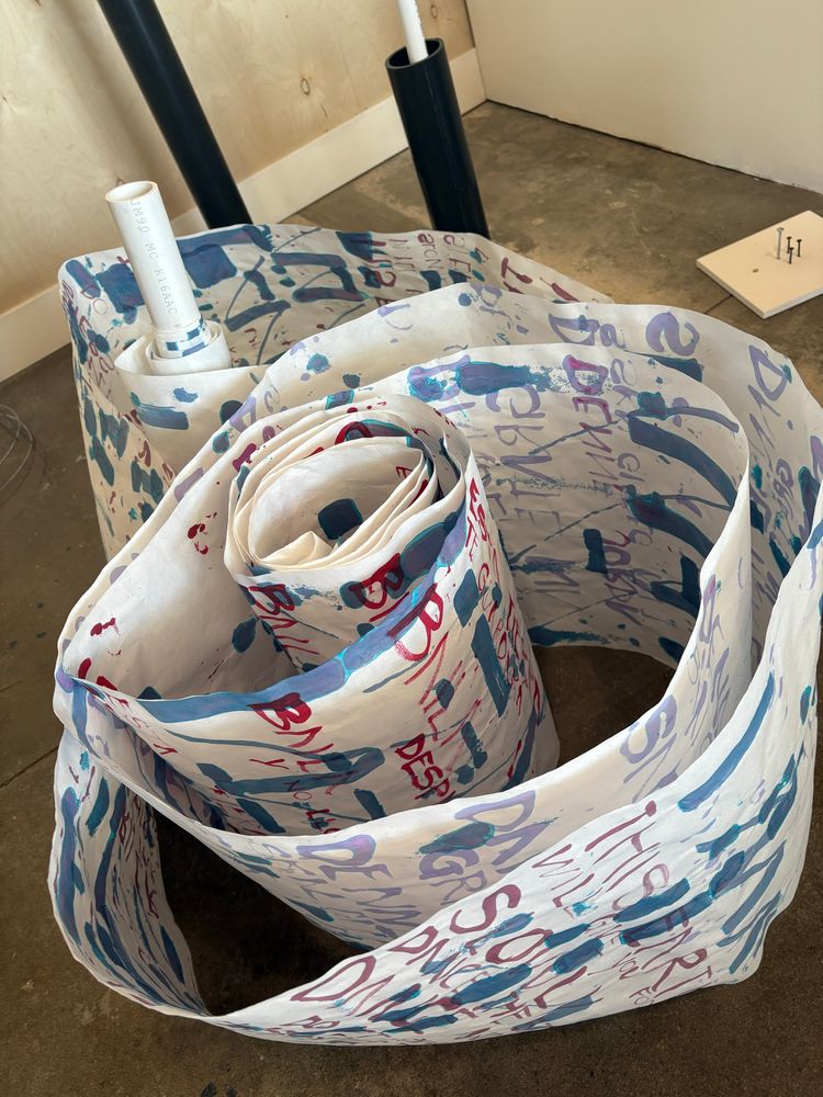 A red, white, blue, and lavender hand painted scroll unfurls to reveal text in Spanish, English, and Norwegian 