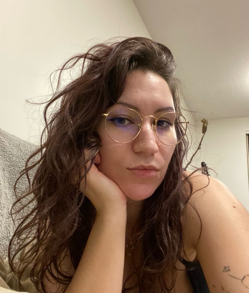 Sam with her chin in her hand sitting stomach down on the couch showing her wavy hair