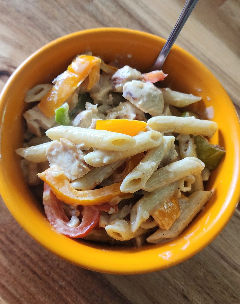An orange bowl with pasta, bell peppers, chicken and cream sauce
