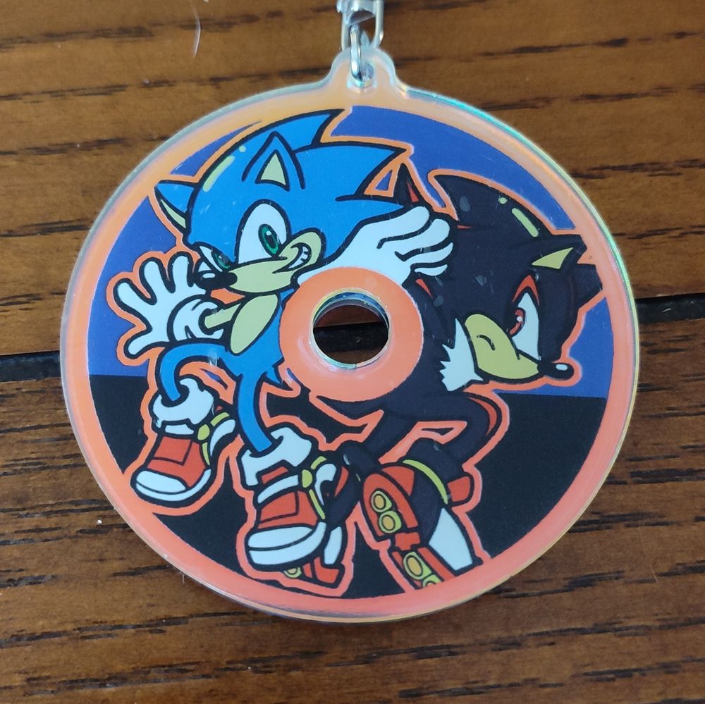 A circular keychain featuring Sonic and Shadow posing together. The keychain resembles a CD, with a hole in the middle
Can't help but notice that Shadow's attention seems to be on Sonic...