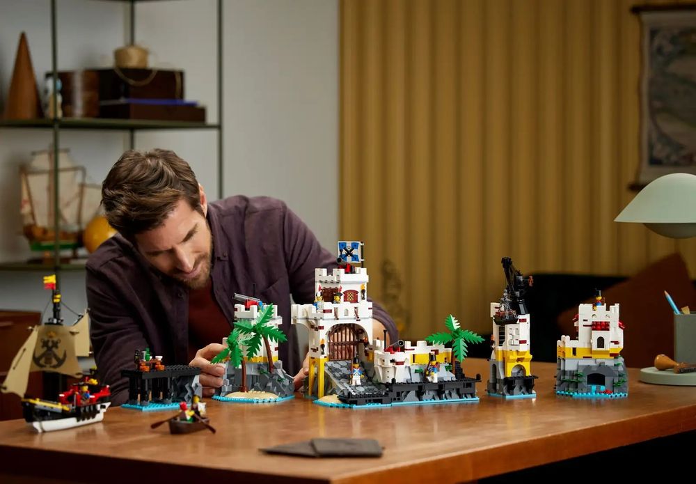 A well-presented man investigating the LEGO Eldorado Fortress (10320) set on a table with a designer lamp