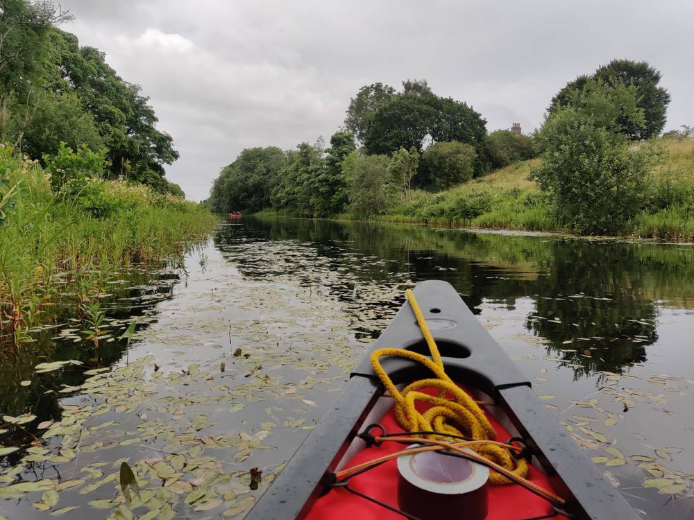 Front of a canoe on a canal surrounded by thick greenery