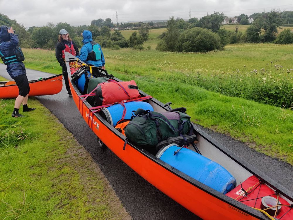 Canoe heavily laden with bags and barrels being carried along a tow path