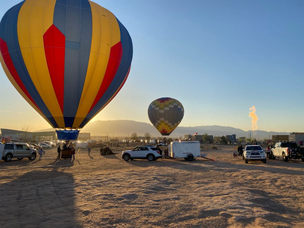 Balloons inflating on a dirt lot with sun rising in distance. 