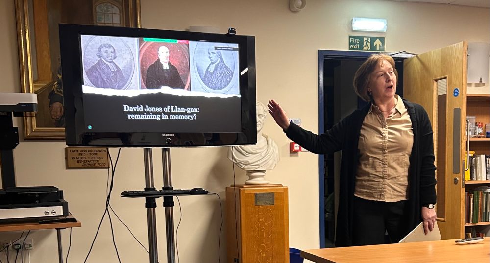 Dr Eryn White presenting a paper, gesturing at a PowerPoint reading ‘David Jones of Llan-gan’ 