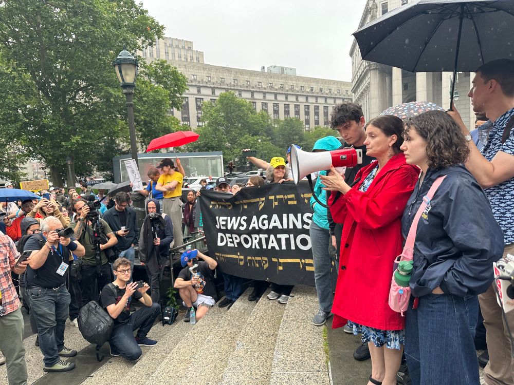 Photo of a rally and press conference taking place outside in the rain. Meg Barnette, Brad Lander‘s wife, is speaking into a megaphone.