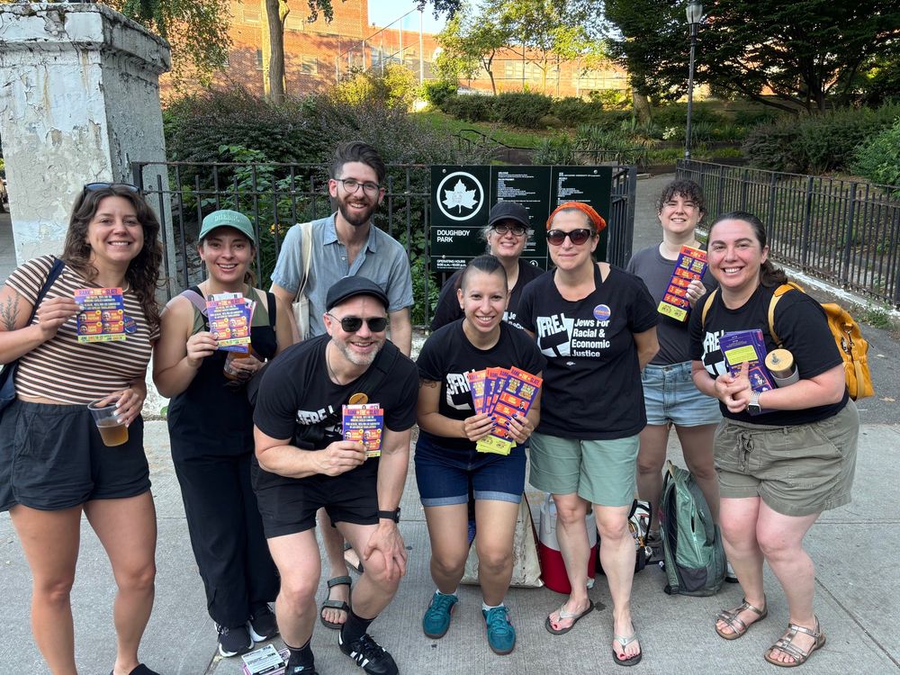 Photo of nine smiling JFREJ members holding Working Families Party campaign lit while standing outside a park in Queens. 