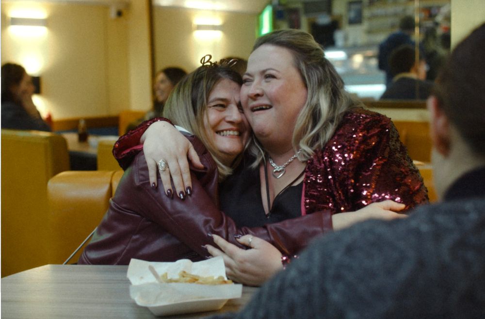Two women hug in a chippie on a hen night