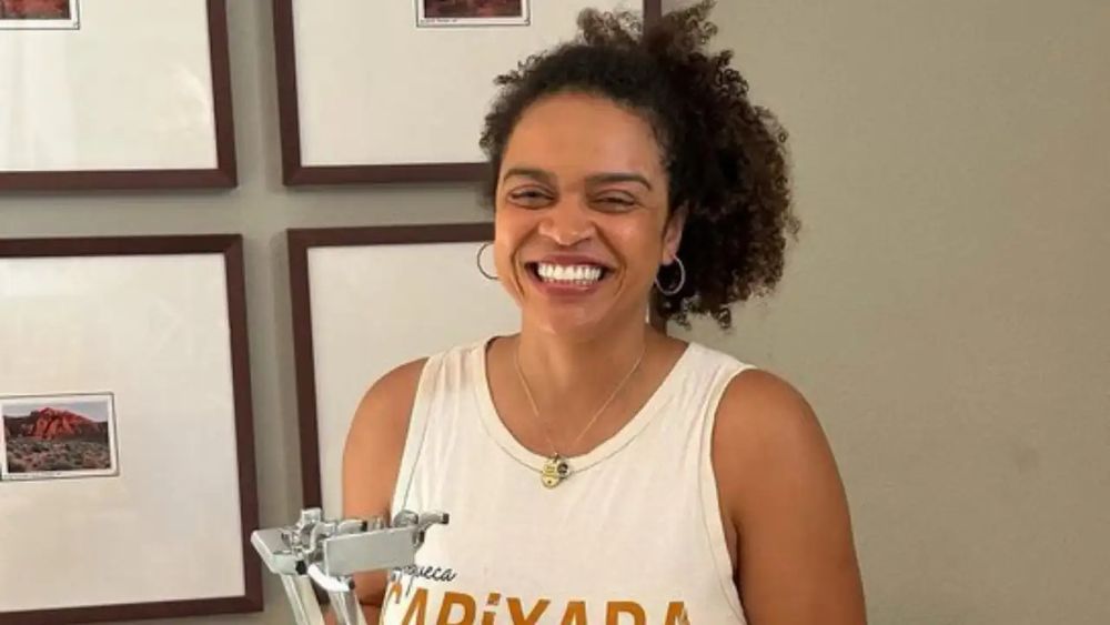 The filmmaker Barbara Gomes Marques. A smiling US-Brazilian woman wearing a white top and standing by a microphone.