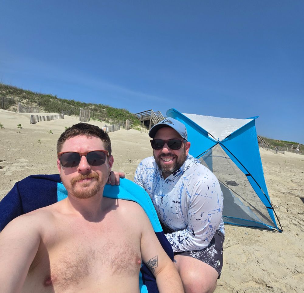 Myself in a chair and Joe crouching behind me for a picture at the beach. Also featuring Joe's shade tent.
