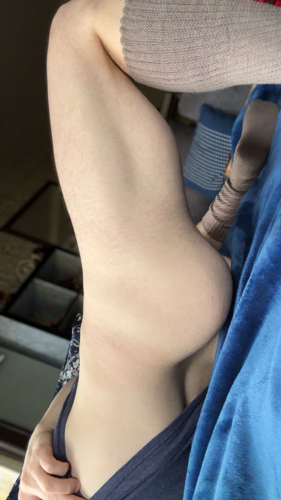 A man on his back on a couch, propping his left hip up and pulling up his shirt showing off his naked waist and ass