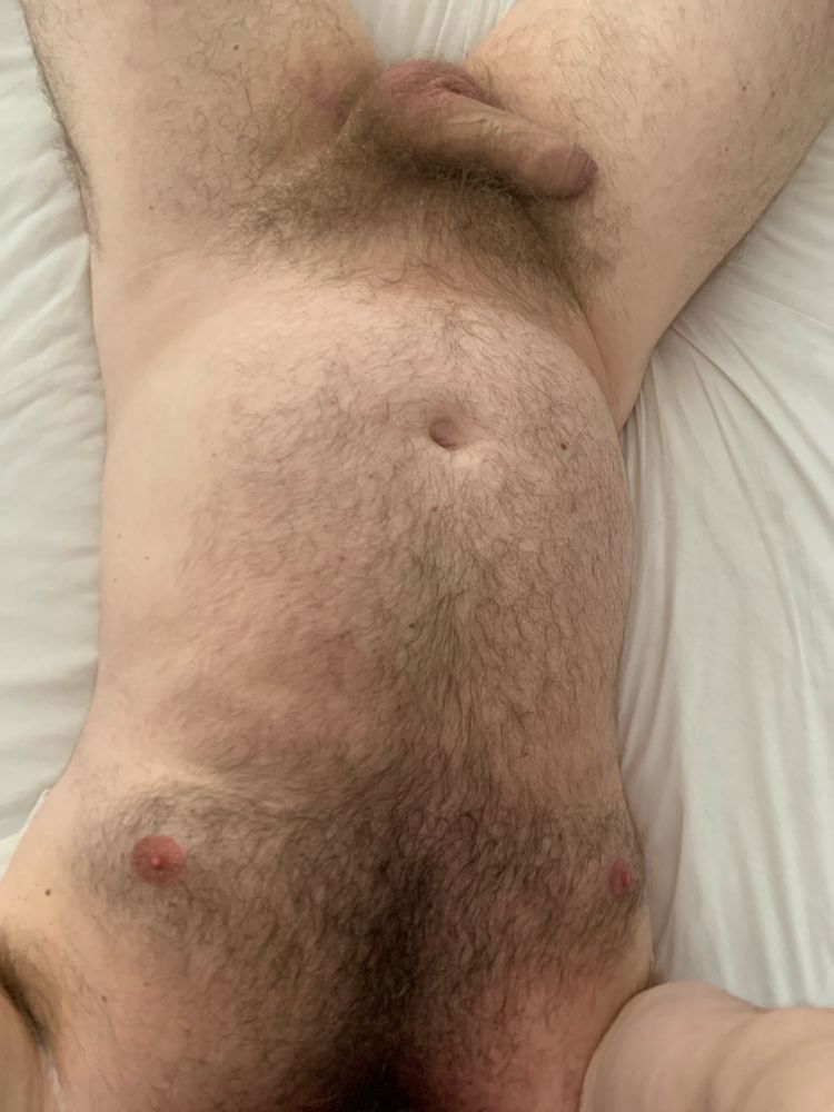 Naked hairy torso on bed with soft cock resting on right thigh
