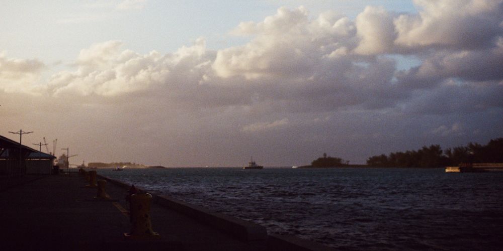 A small boat sits in the middle of the bay as the sun sets and clouds come in