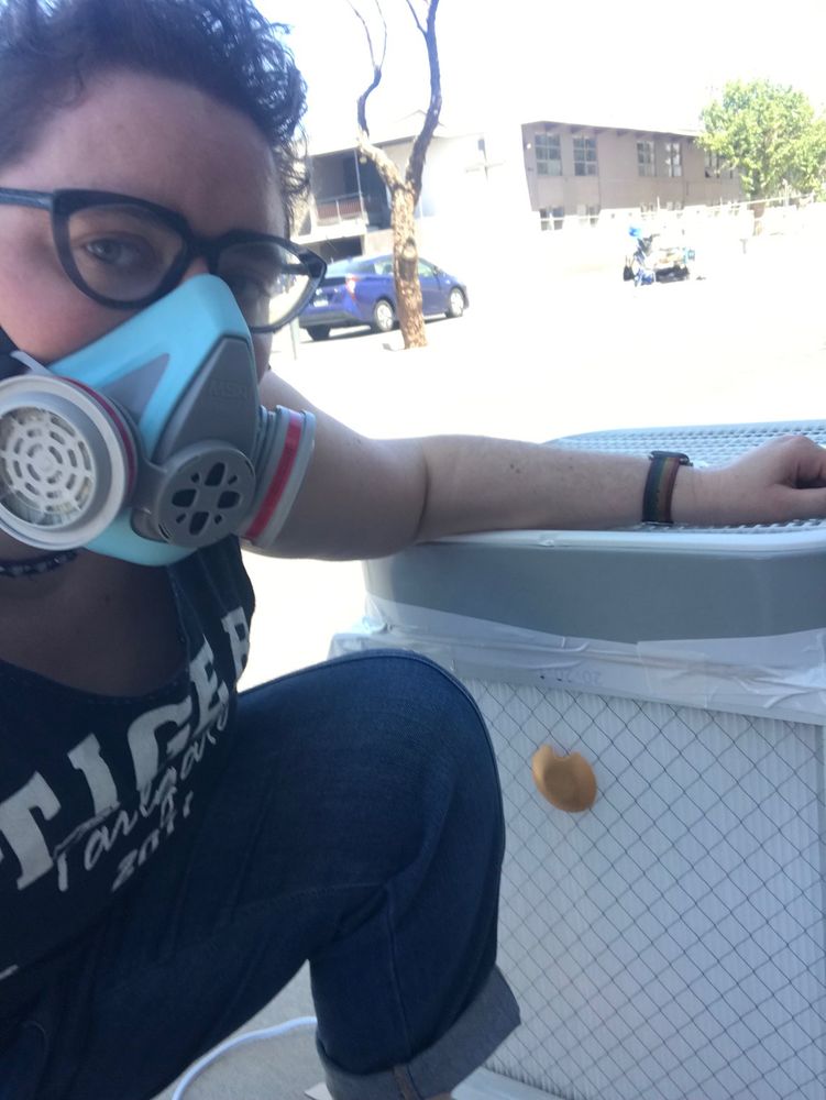 A person with short brown hair, glasses, and a teal respirator posing next to a Corsi-Rosenthal Box