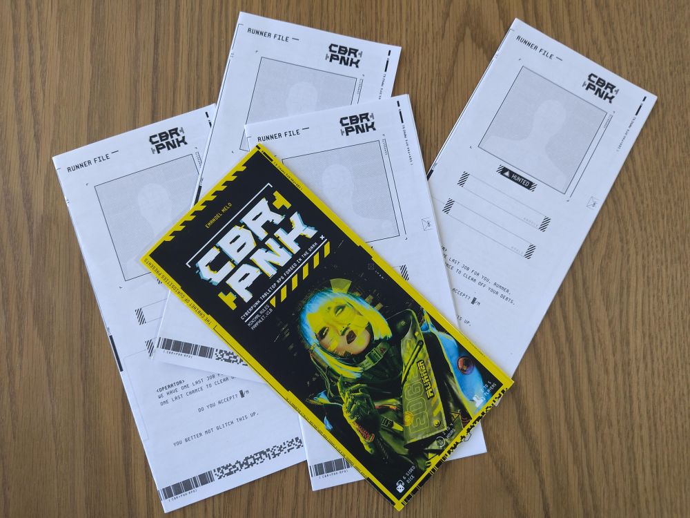photo of the first version of CBR+PNK printed out, GM pamphlet in color, and 4 player pamphlets in black and white