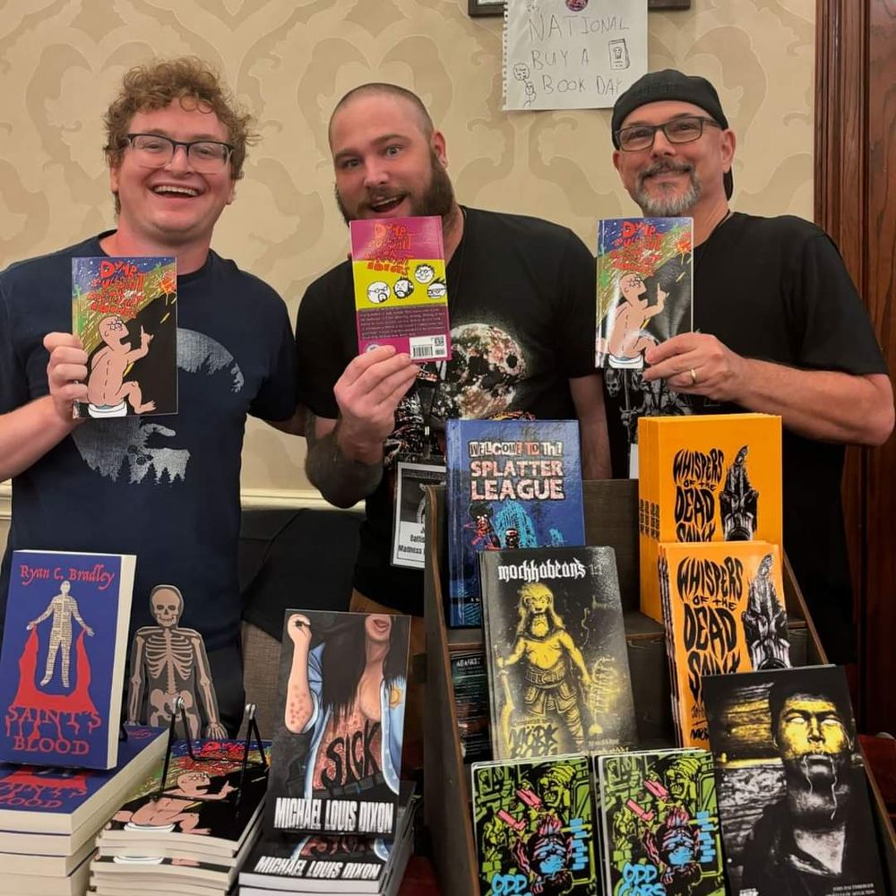 L to R: me, John Baltisberger, and Michael Louis Dixon holding up copies of our co-written book, Dumb Bullshit for Brilliant Idiots in front of our table at Armadillocon 2024. 