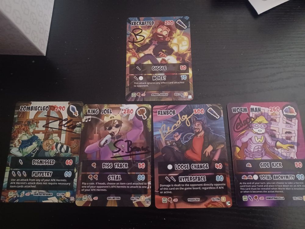 5 signed hermitcraft tcg cards laid side by side on a table. Xbcrafted on top. Then left to right, zombiecleo, King joel, rendog, and worm man.