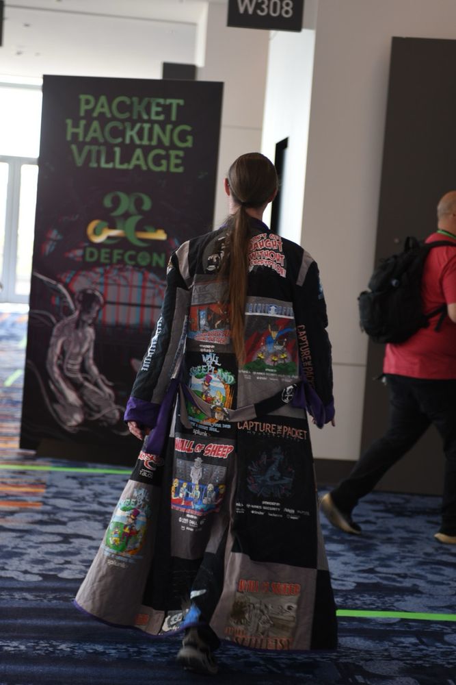 DC33 attendee heading to the Packet Hacking village wearing a duster liberally festooned with PHV graphics.