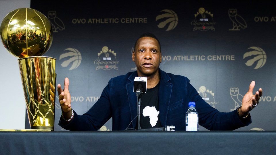 Masai Ujiri sitting next to the Larry O’Brien trophy with this arms and hands spread out