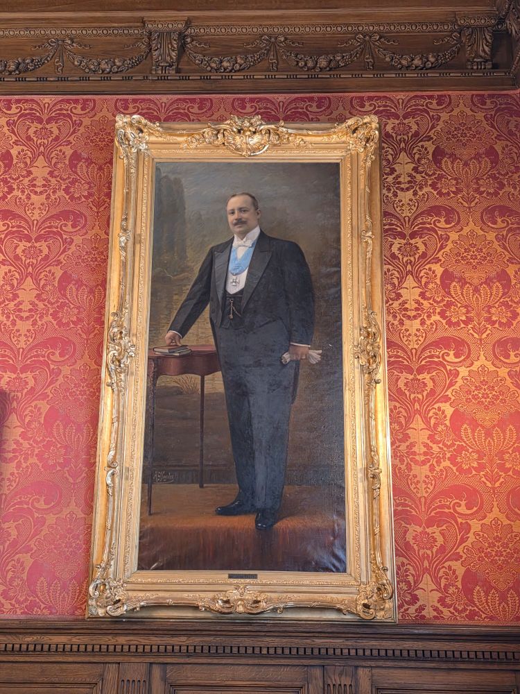 A painted portrait of Simon Patiño in a gold frame. He is stout, standing, wearing a business suit.