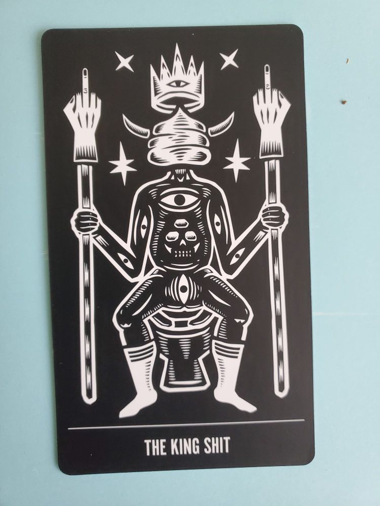 THE KING SHIT. A man with a turd for a head is sitting on a toilet and holds two staffs, each with a hand giving the middle finger on top.