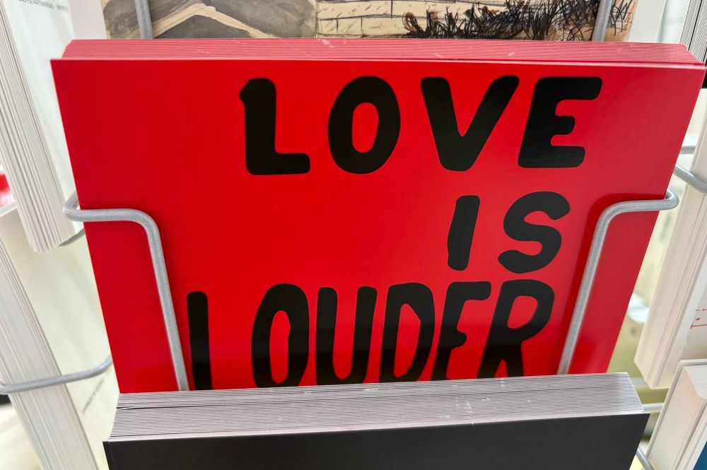 Postkarte mit schwarzem Aufdruck „love is louder“ auf rotem Grund.