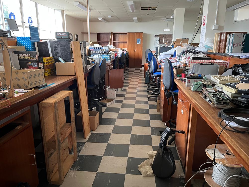 The Digital Systems laboratory with wooden benching and a checkerboard tiled floor, with lots of old historic electronics bits and pieces to sort through and dispose of. 