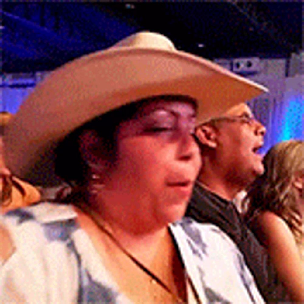 a woman wearing a cowboy hat is sitting in a crowd of people