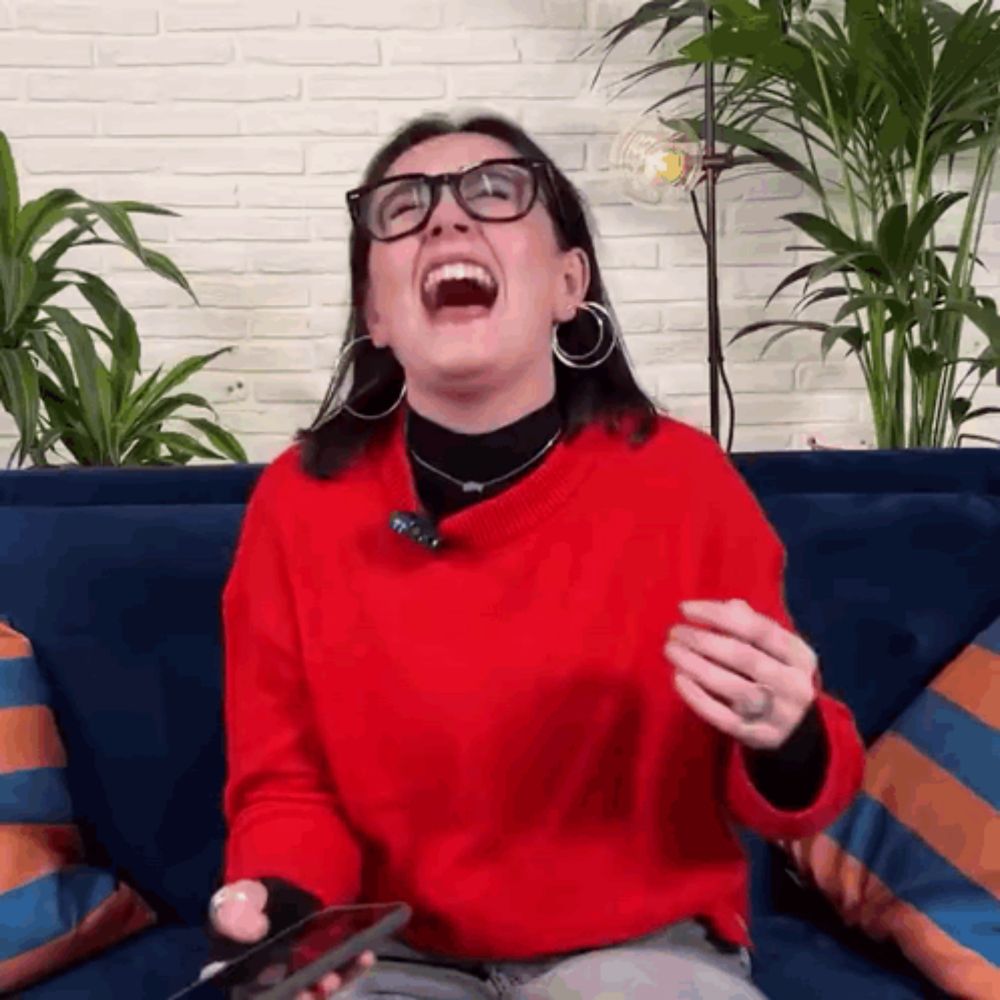 a woman in a red sweater and glasses is laughing while sitting on a couch .