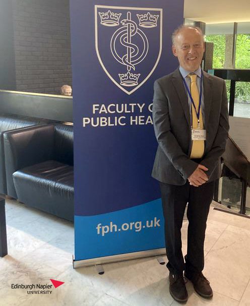 Adrian Davis standing in front of a banner of the FPH logo