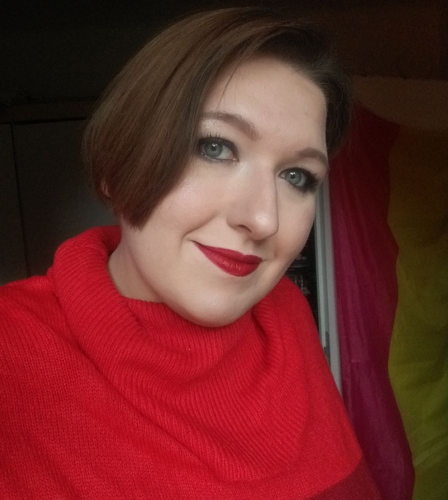Selfie of yours truly, a very fair-skinned femme with gray eyes showing off my new haircut, an asymmetrical pixie/bob kinda thing? I'm in a red turtleneck dress and wearing matching lipstick.