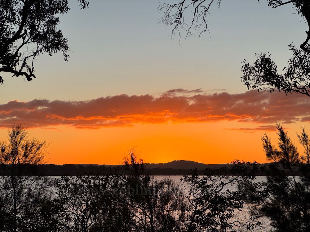 A burning orange sunset taken across a lake, with a low hanging cloud reflecting the orange 