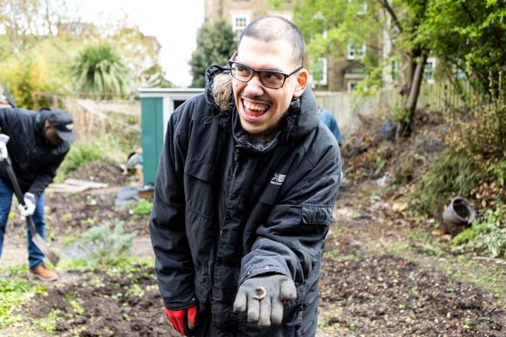 Man in an allotment smiling and holding out his hand with a worm on it.