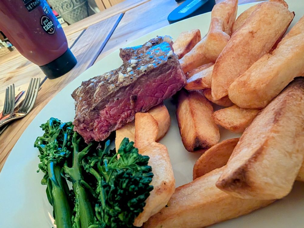 A cooked medium rare steak with chips and tender stem broccoli