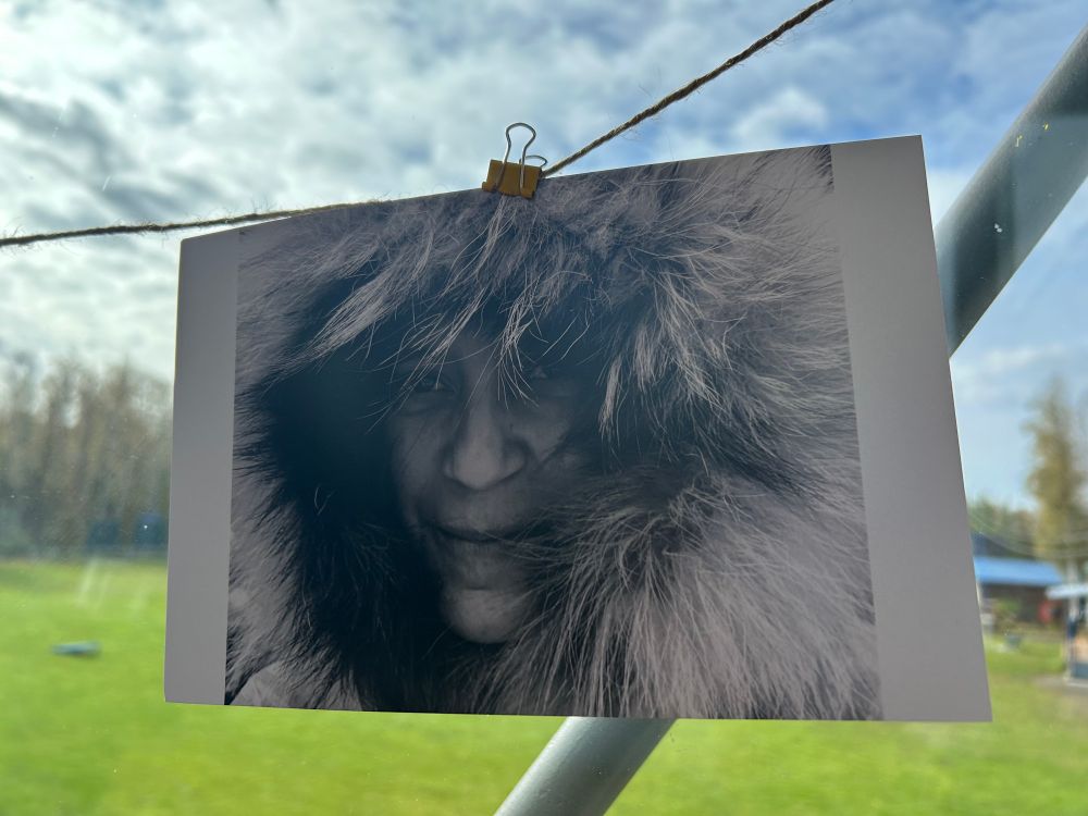 Photograph of a woman in an Arctic parka hanging in front of a window. 