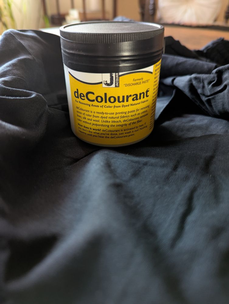 A bottle of decolourant (a liquid used to remove color from fabrics) sits on a black cloth.