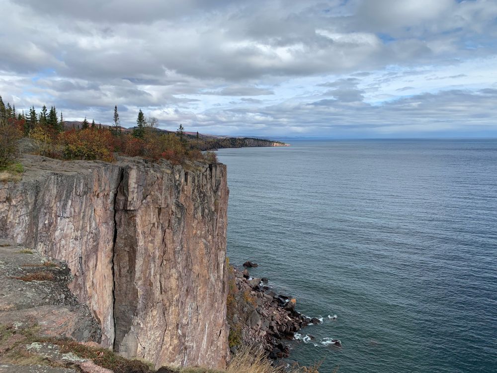 The shoreline laps far below a tall imposing cliff of solid stone under cloudy skies.