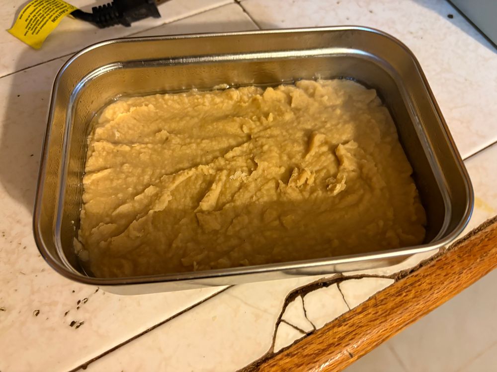 A metal container filled a third of the way with still warm garbanzo ( or chickpea) tofu. 