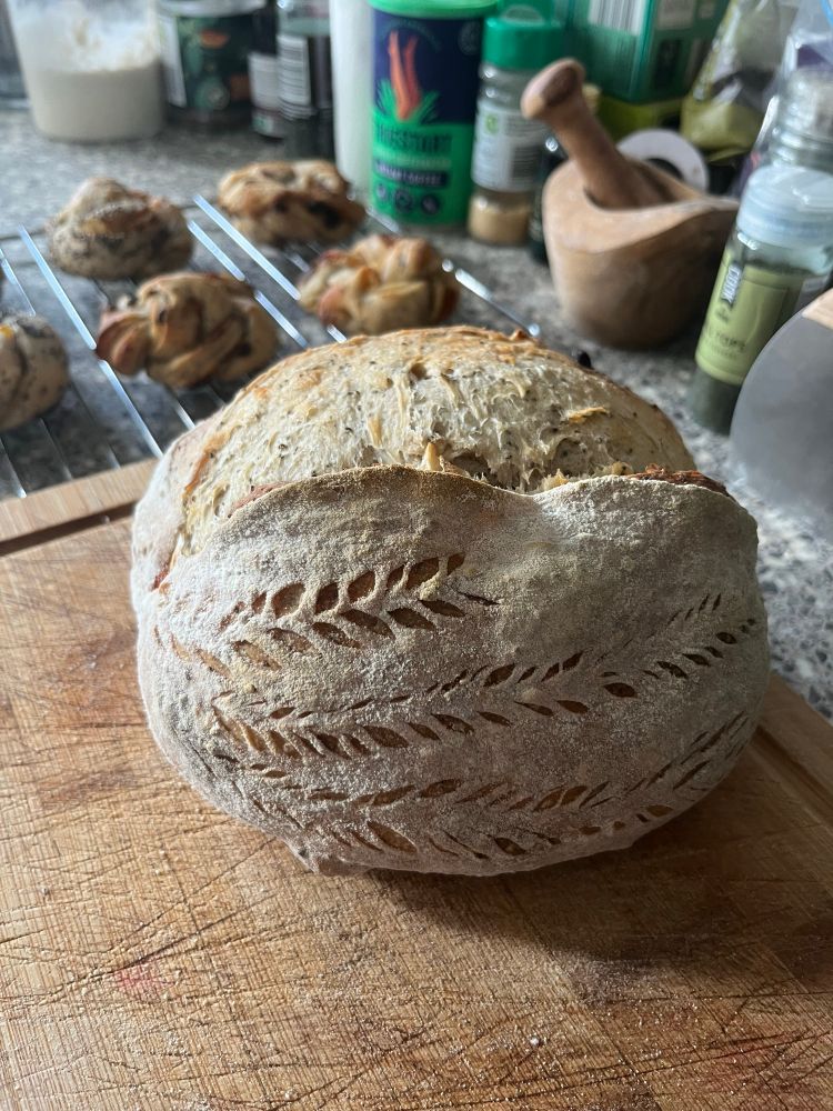 Apricot and chia seed baked sourdough loaf with a wheat stalk scoring pattern on a wooden chopping board 