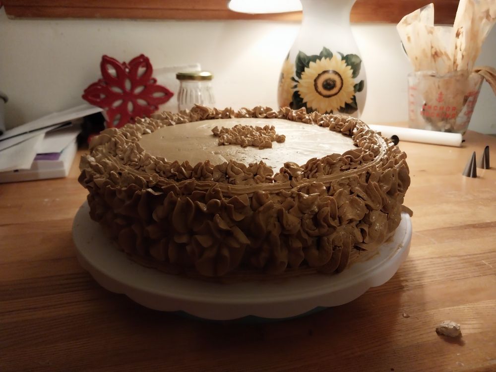 View of cake from side.  Is decorated using flower shaped piping tips to so the sides are covered in coffee flowers