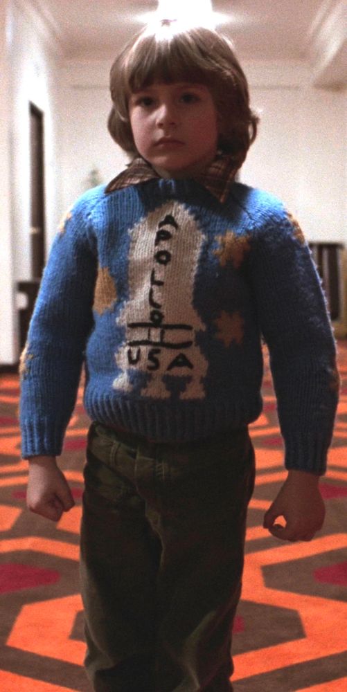 Danny Torrance in “The Shining” wearing a blue knit sweater with the words “APOLLO USA” on a white representation of a Saturn V rocket.