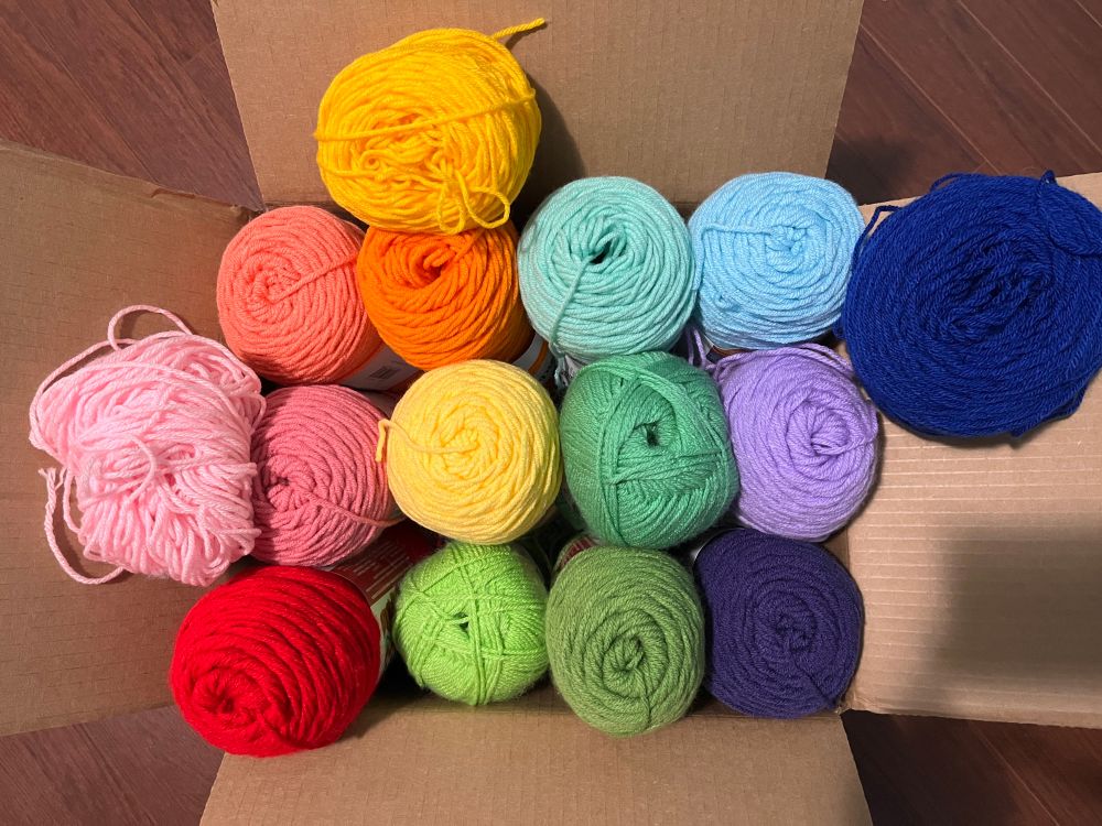 box full of yarn of various colours, poorly organized in rainbow order