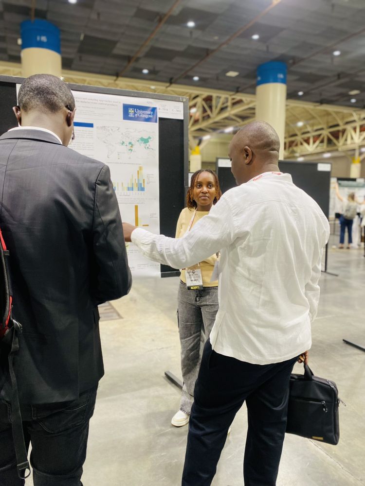 Victoria Githu, researcher at the Ifakara Health Institute and PhD student at the University of Glasgow, is shown talking to 2 attendees at the ASTMH 2024 conference who are visiting her poster.