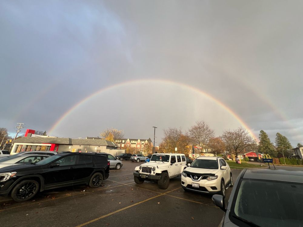 Double rainbow captured in suburban parking lot over shopping centre in late afternoon while cloudy and raining. 