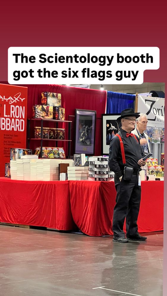 Scientology booth at comic con with an older man in suspenders standing in front 