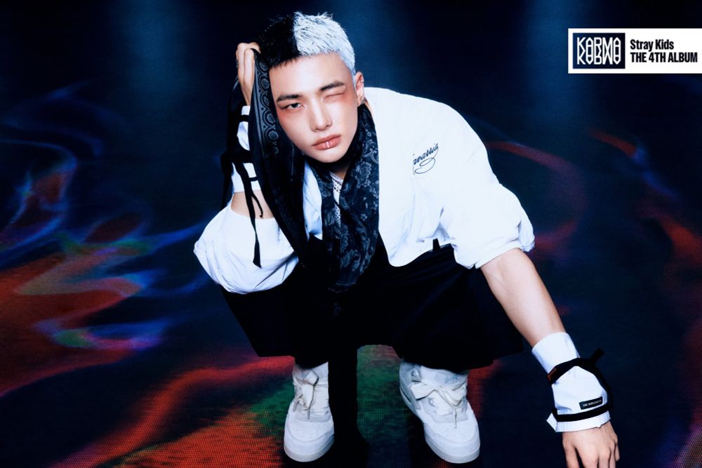 Hyunjin for Karma. He's crouched and staring at the camera, one eye closed. His hair is black and white a la Cruella.