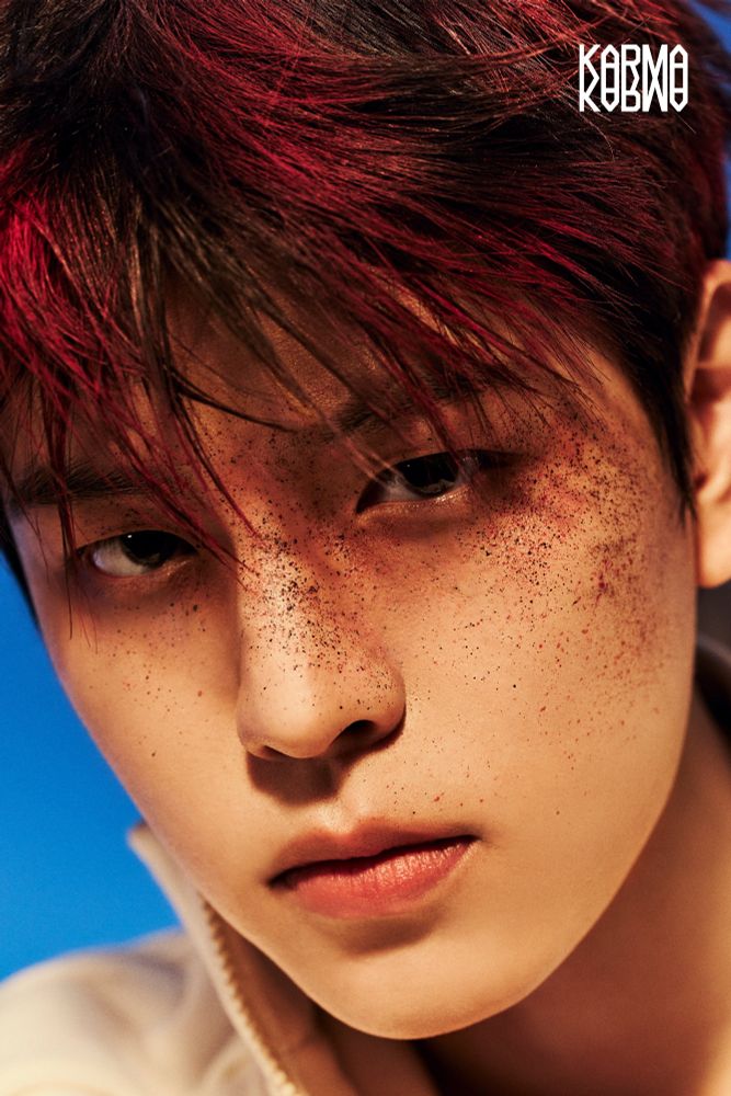 Seungmin for another Karma photoshoot. It's a close-up of his face. He has red sprayed on his hair and there's red and black dust/soot/smth covering his face, specifically his nose and high on his cheek and around the eyes. 