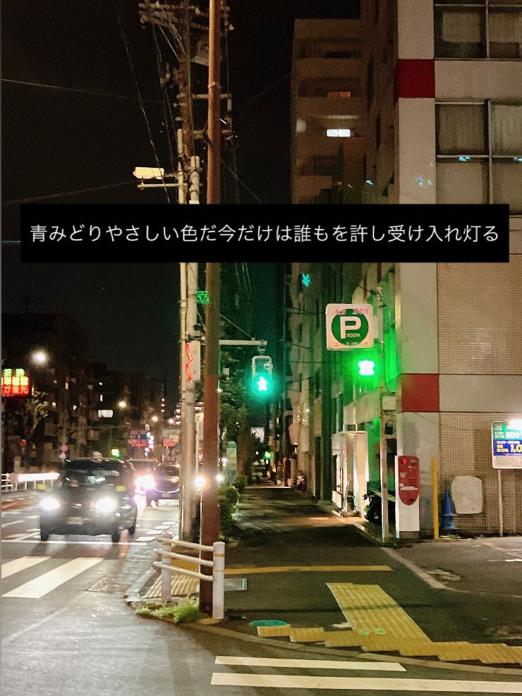 夜の街角の写真。横断歩道の青信号と、駐車場の「空」表示が並んでいる。中央に白文字で「青みどりやさしい色だ今だけは誰もを許し受け入れ灯る」と記されている。
